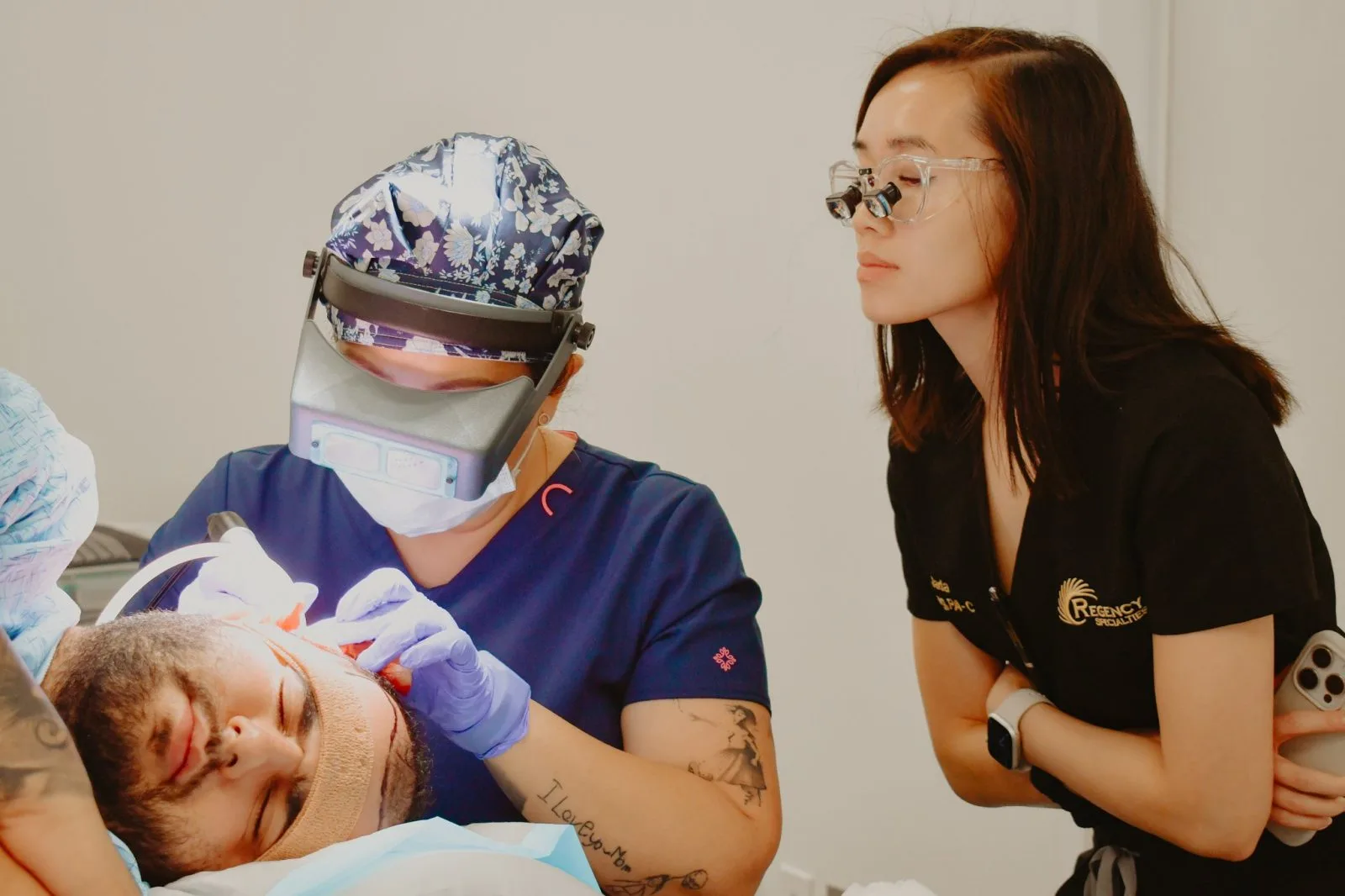 Regency Specialties provider wearing surgical loupes and headlamp examines patient's face while colleague observes